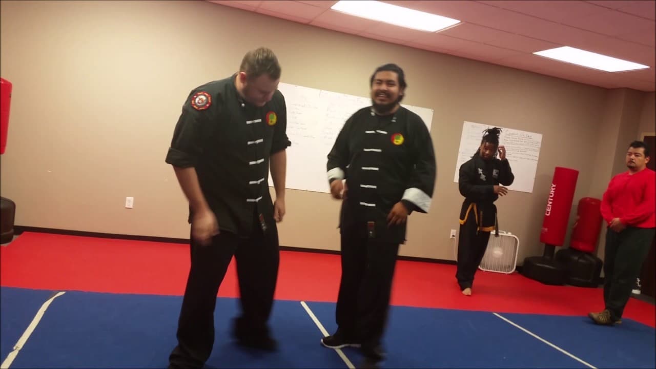 Two instructors in black kung fu uniforms working on the red mat