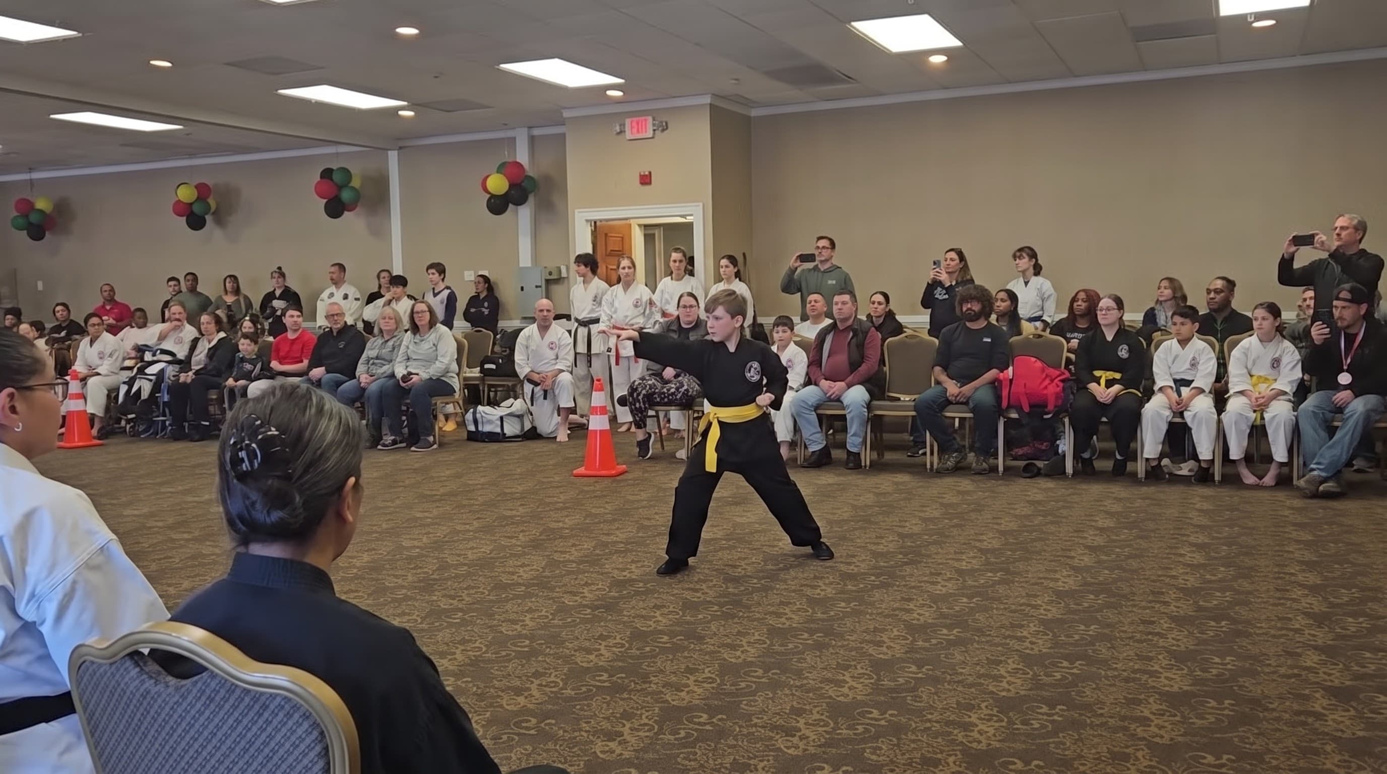 A young student in a yellow sash performing a form at a tournament