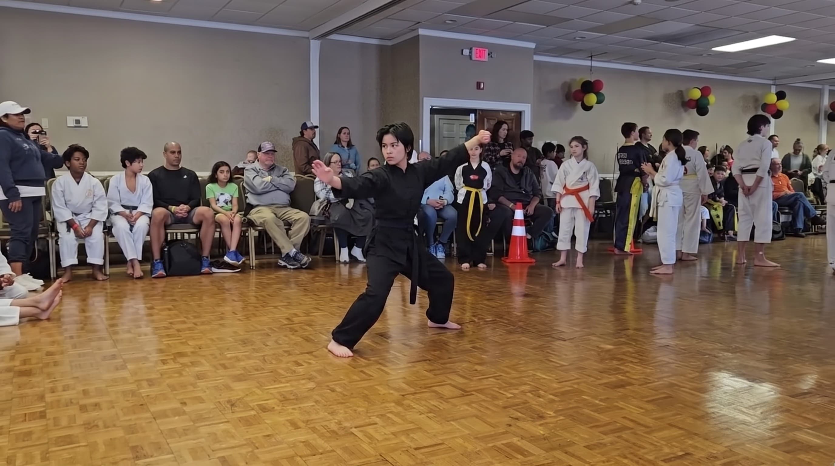 A teenage student performing a form in front of seated karate students