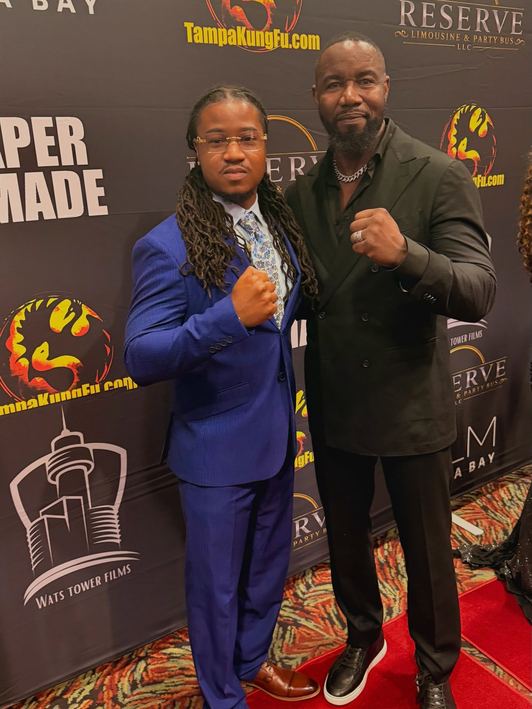 Cequence Henry in a blue suit with Michael Jai White on the Paper Made step-and-repeat